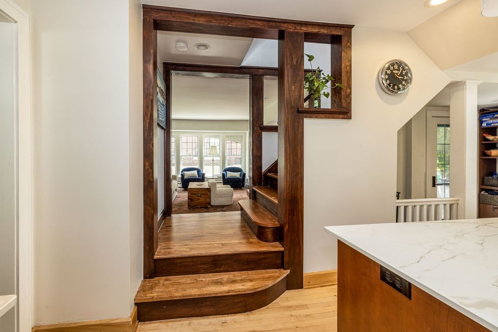 An elevated entryway with dark wood trim and steps leading to a living room seen through a doorway, beside a kitchen island.