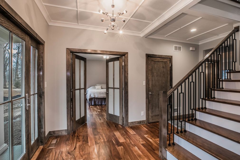 An entryway with hardwood floors, a staircase with a black railing, a doorway leading to a bedroom, and glass doors.