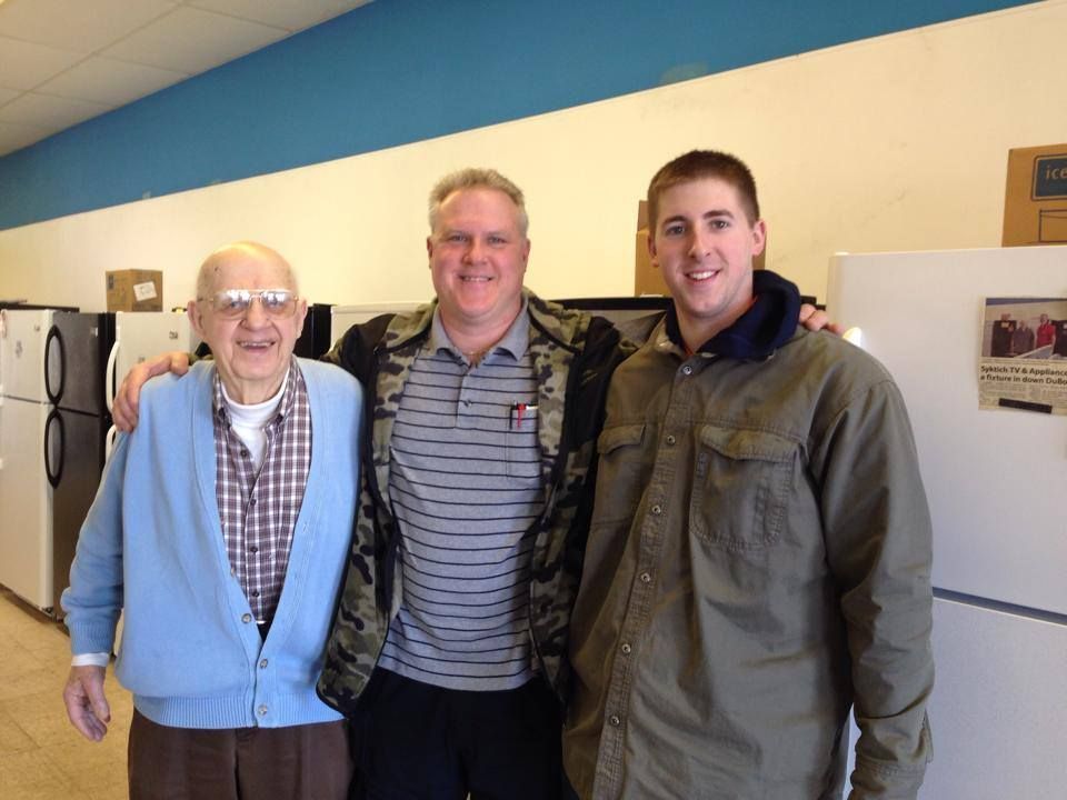 Three men are posing for a picture in front of a refrigerator