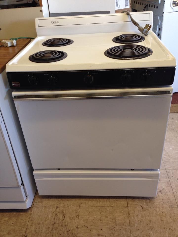 A white stove with four burners is sitting on a tiled floor.