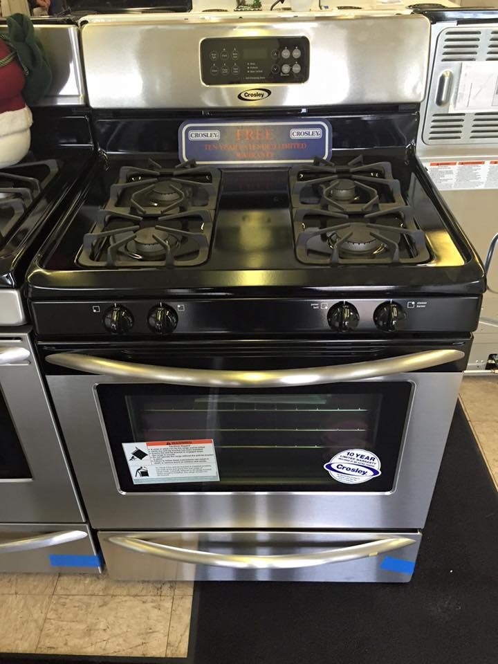 A stainless steel stove with a black top is sitting on a tiled floor.