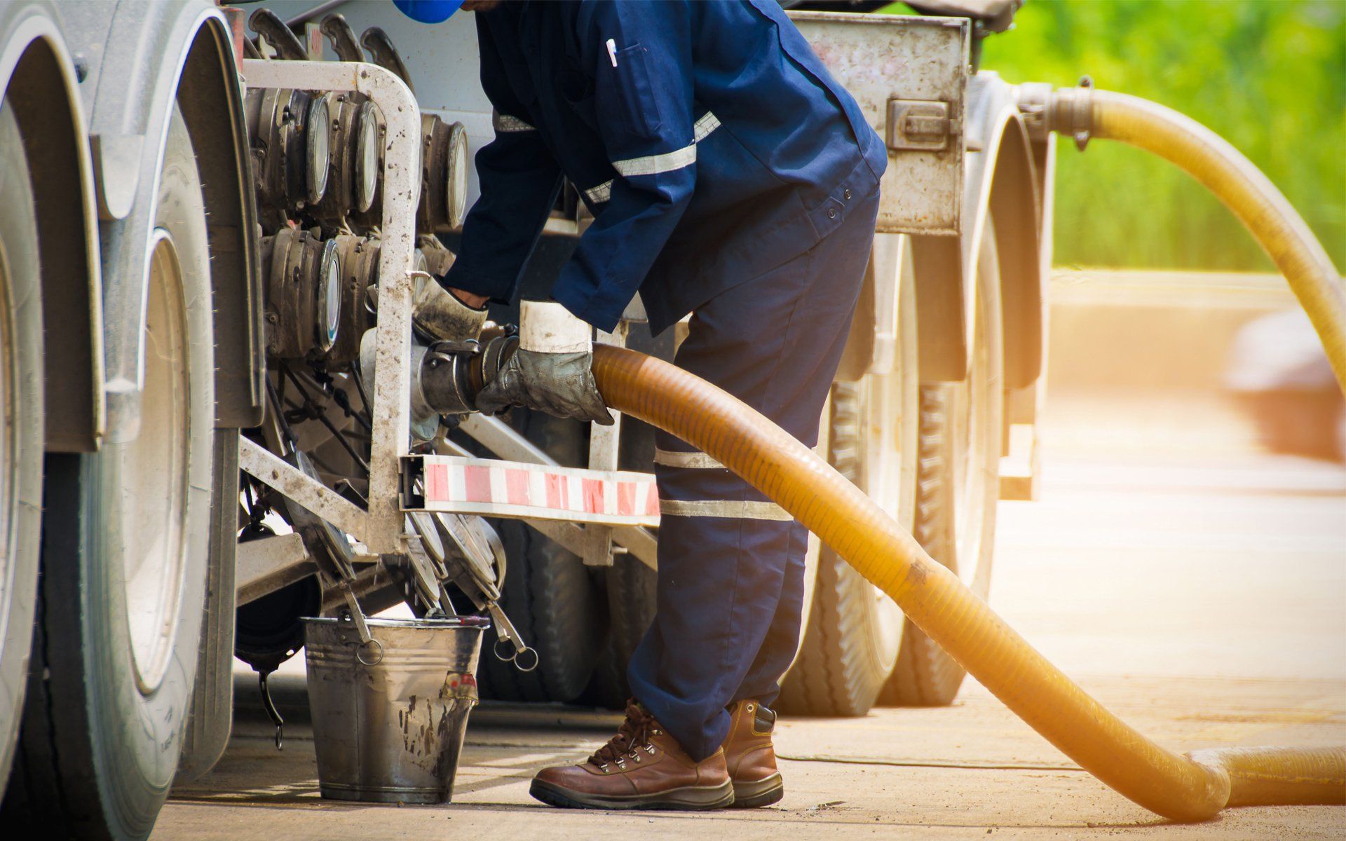 Worker in blue jumpsuit attaching hose to tanker truck.