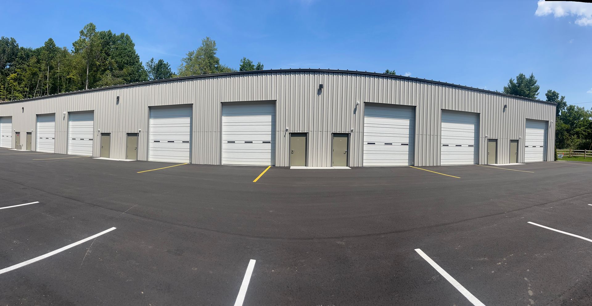 Gray metal building with multiple garage doors; asphalt parking lot with white lines.