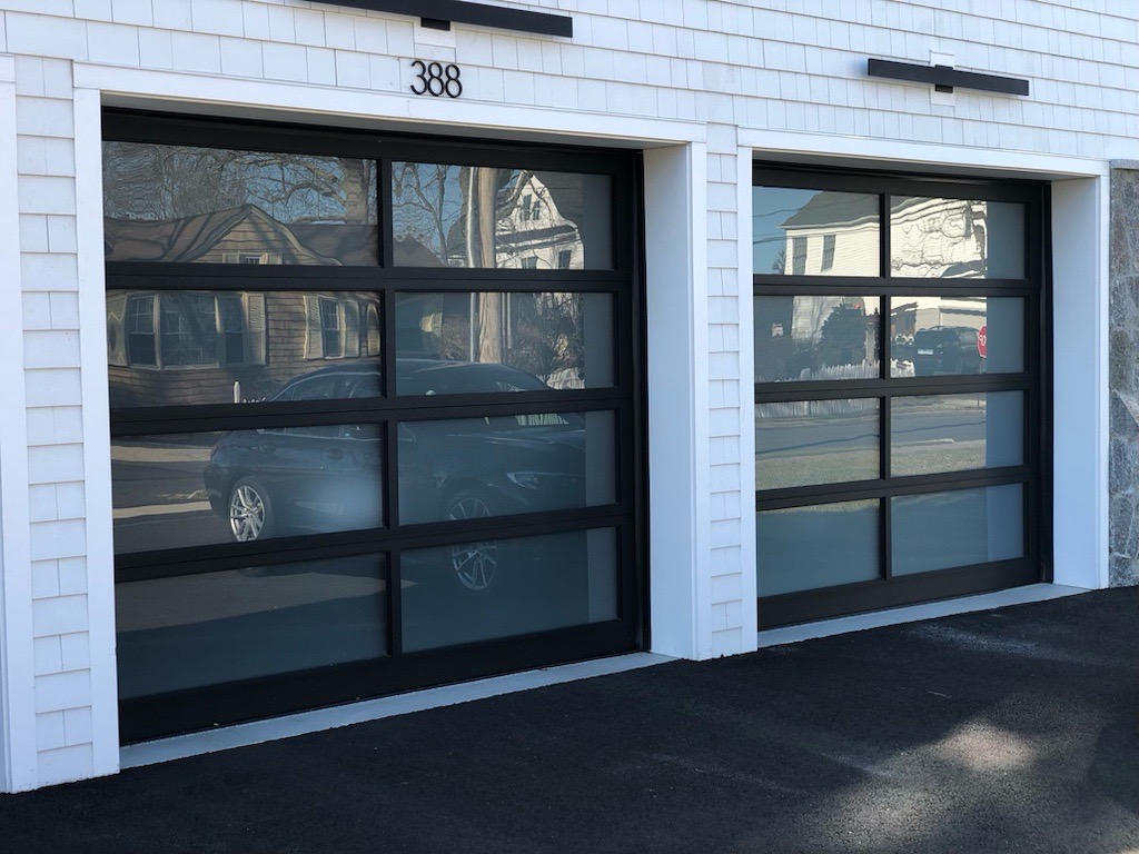 Two black-framed glass garage doors with reflections, next to white siding.