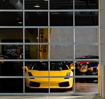 Yellow Lamborghini sports car behind a glass garage door at a dealership.