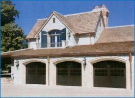 Three-car garage with arched doors and upper level with arched window, light-colored exterior, brown roof.