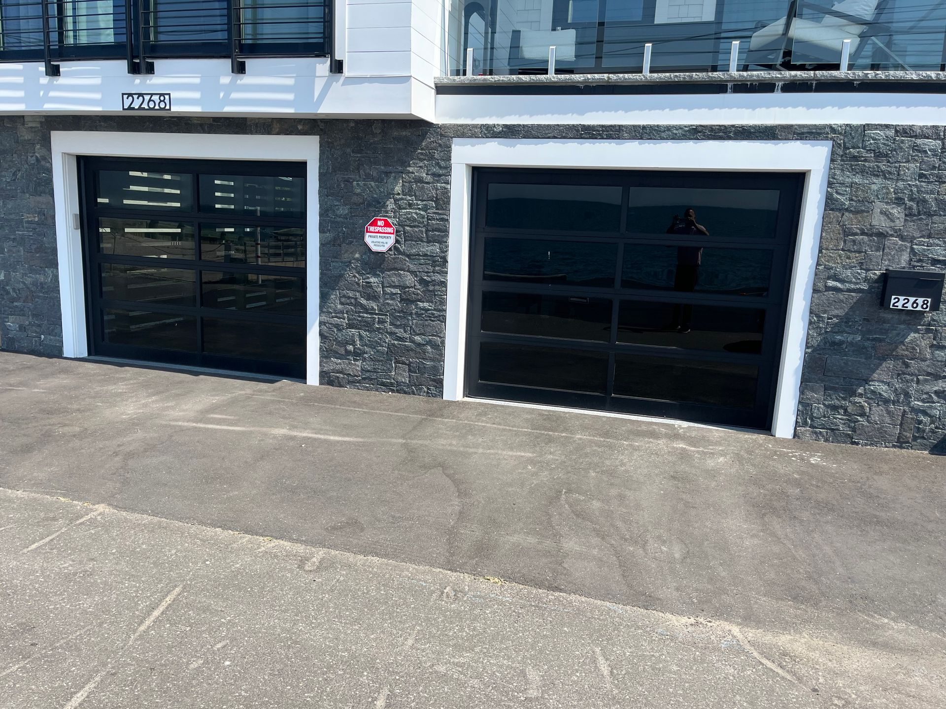 Two black garage doors with glass panels on a gray stone exterior, driveway.