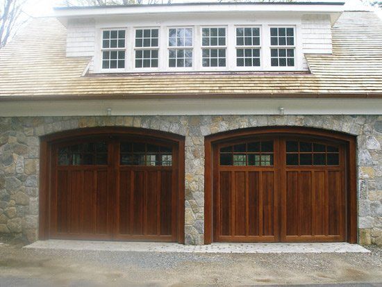 Two wooden garage doors with stone facade and dormer windows above.