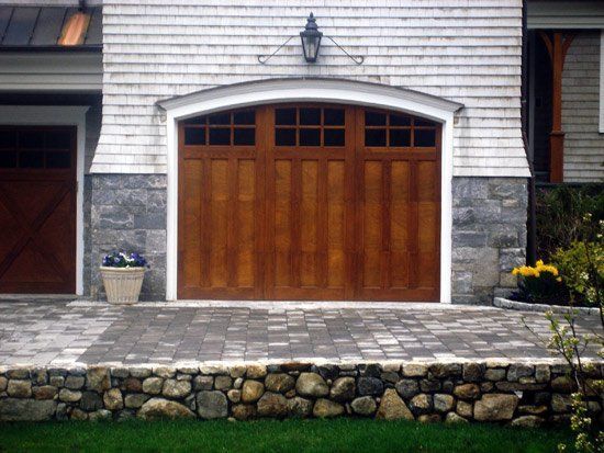 Wooden garage door with arched top, brown with white trim, gray stone base.