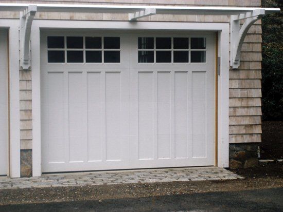 White garage door with windows, flanked by decorative brackets, in a wooden-shingled building.