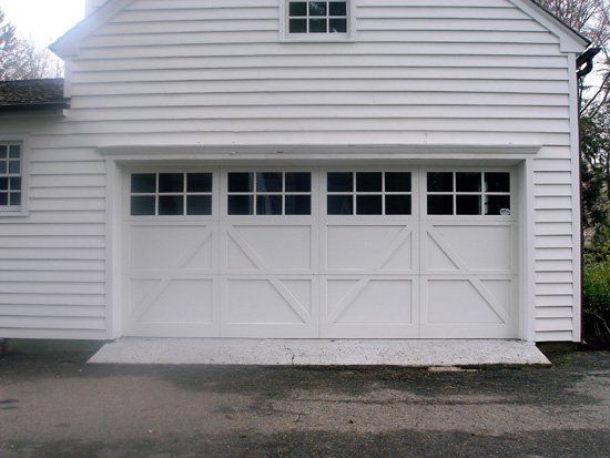White garage door with windows, angled supports, and textured concrete ramp.