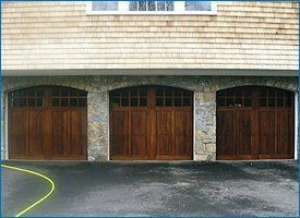 Three wooden garage doors under a light-brown shingled roof and stone facade.