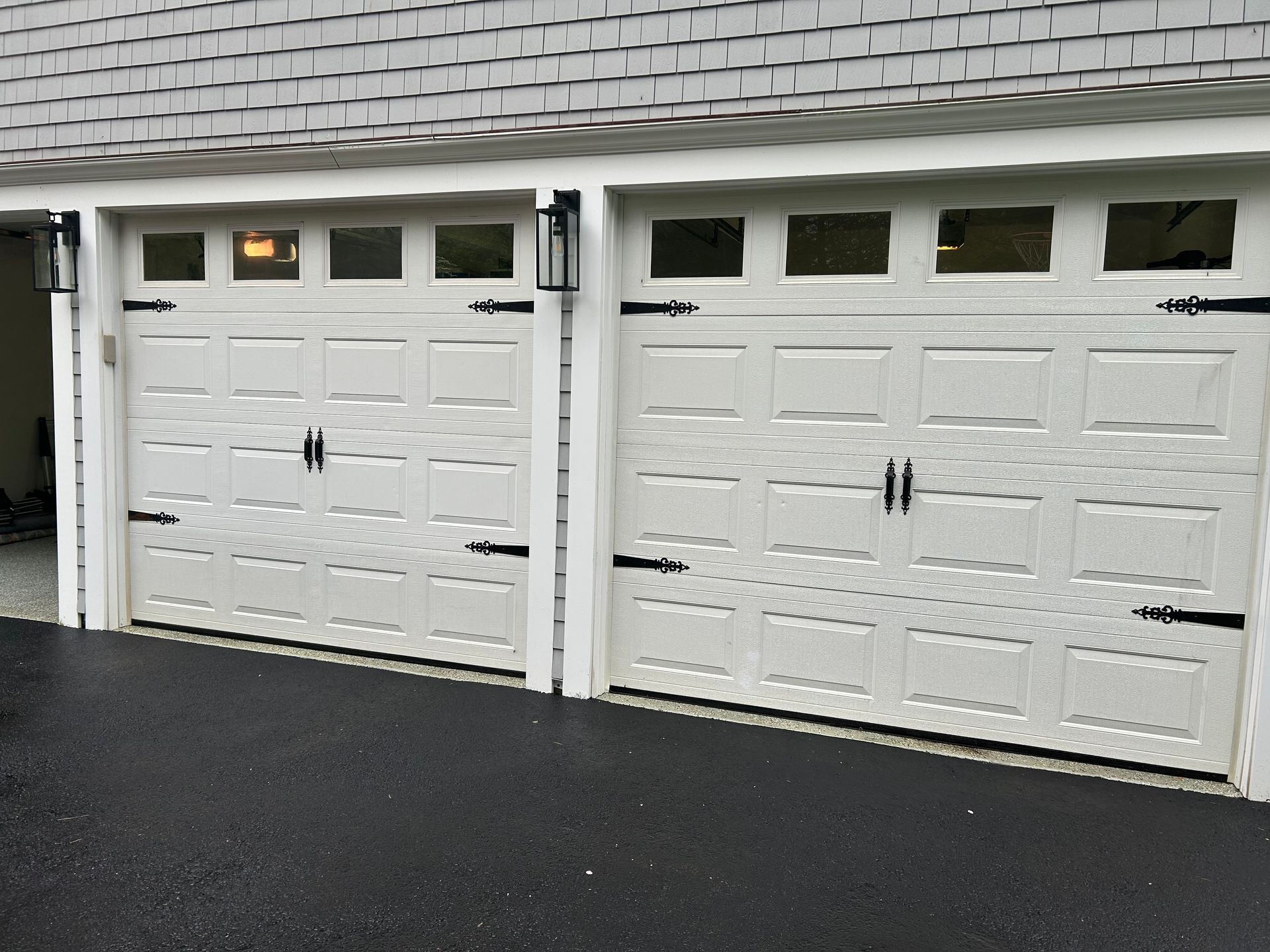 Two white garage doors with black hardware and lights above, set against a gray roof.
