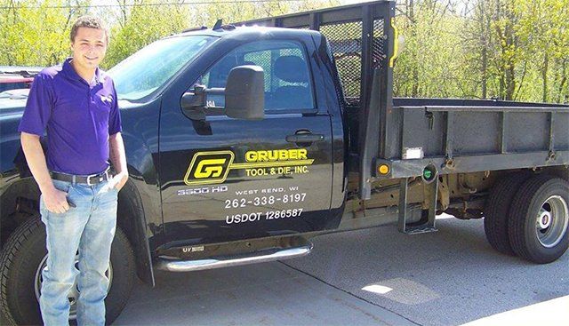 A man in a purple shirt is standing next to a dump truck