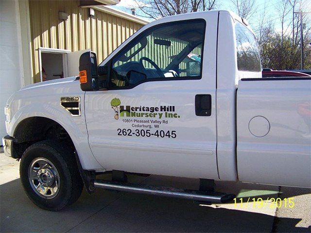 A white heritage hill nursery truck is parked in front of a building