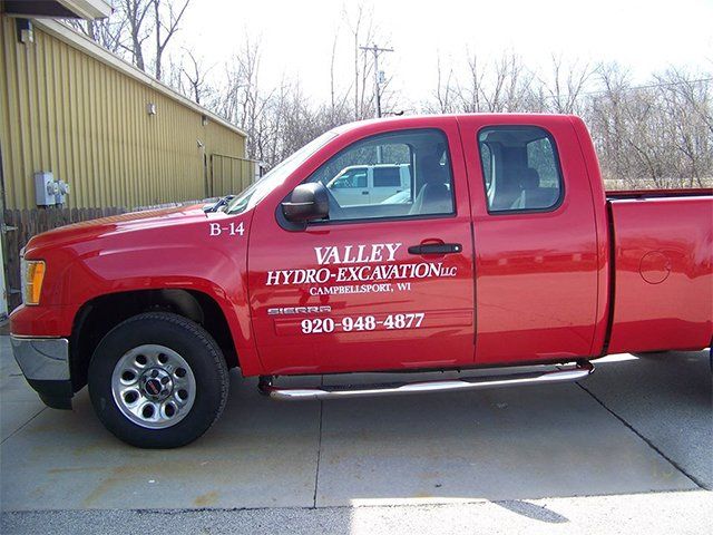 A red valley hydro excavation truck is parked in front of a building