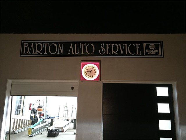 A sign for barton auto service hangs above a clock
