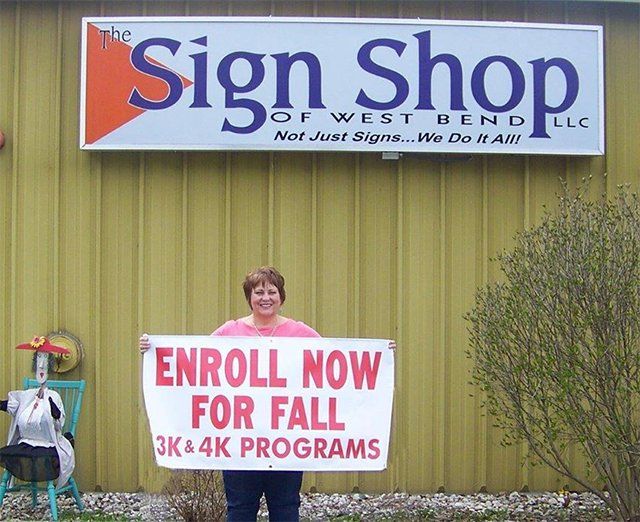 A woman holding a sign that says enroll now for fall