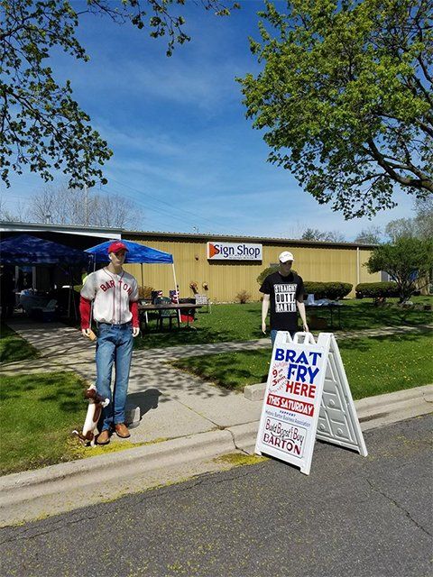 A man standing next to a sign that says brat fry here
