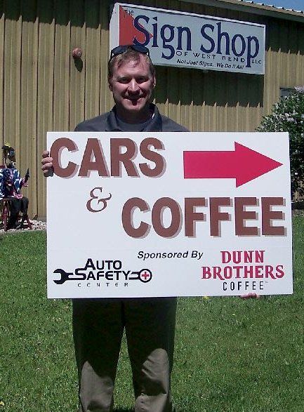 A man is holding a sign that says cars and coffee