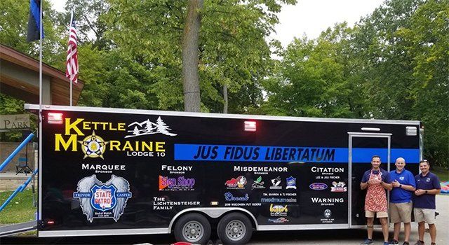 A group of people standing in front of a trailer that says kettle migraine