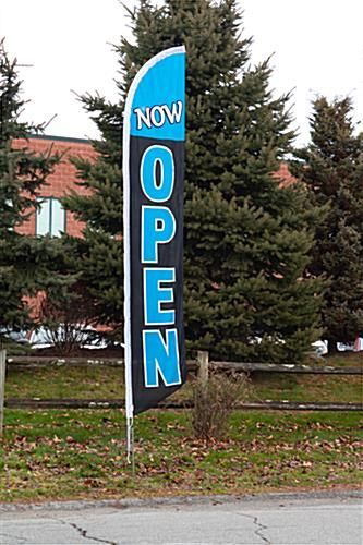 A black and blue flag that says `` now open '' is sitting on the side of the road.