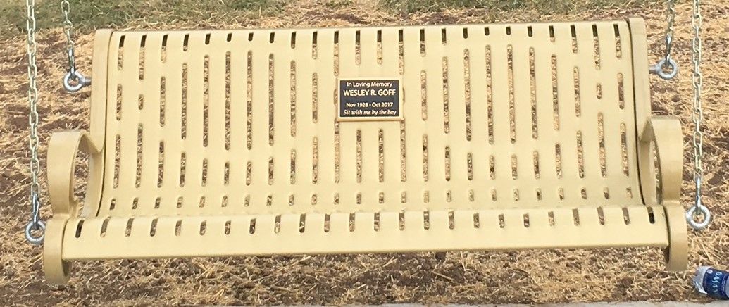 A yellow bench with a plaque on it is sitting on the ground.