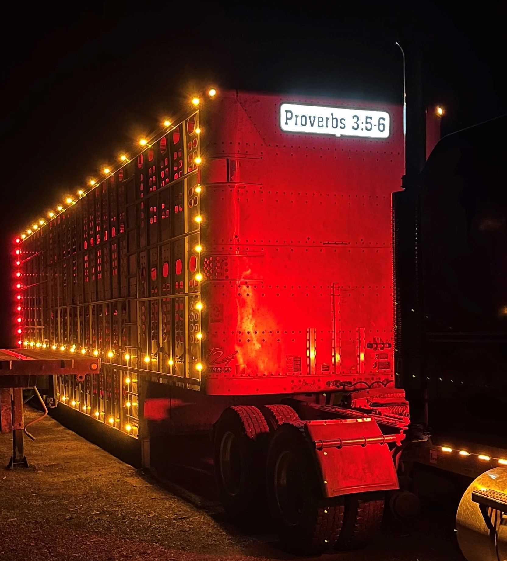 A large red semi truck is lit up at night.