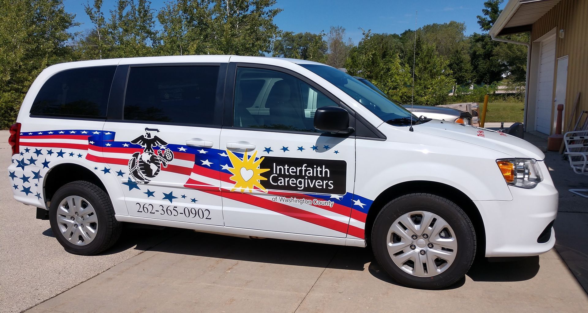 A white van with an american flag on the side is parked in front of a building.