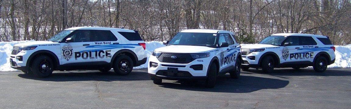 Three police cars are parked on the side of the road in the snow