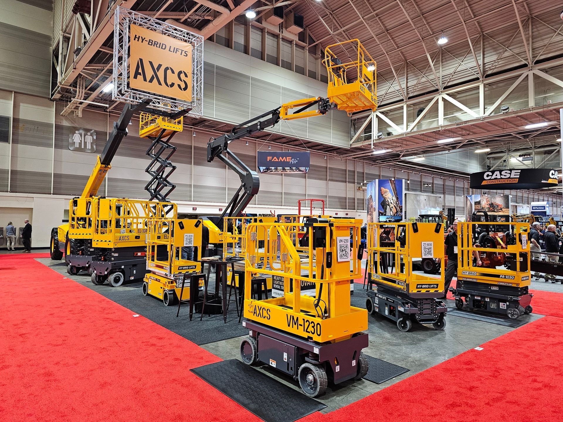 Yellow aerial work platforms on a red carpet at a trade show. AXCS sign overhead.