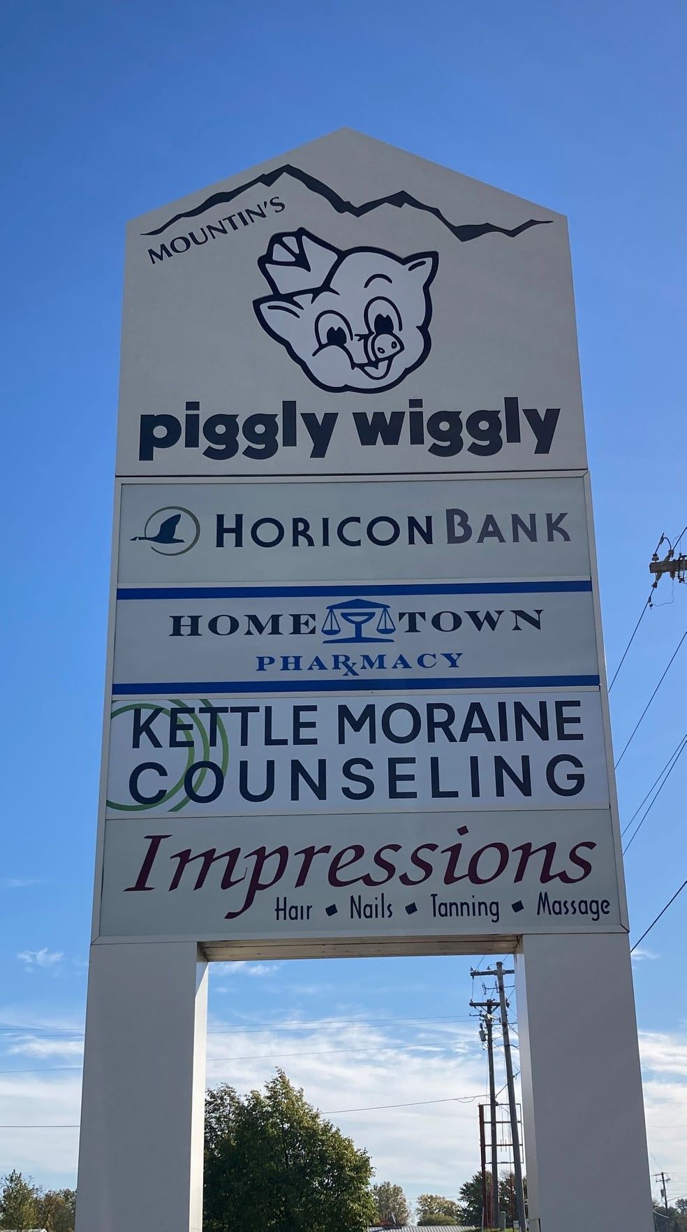 Sign for a shopping center with businesses, Piggly Wiggly, Horizon Bank, Hometown Pharmacy, Kettle Moraine Counseling, and Impressions.