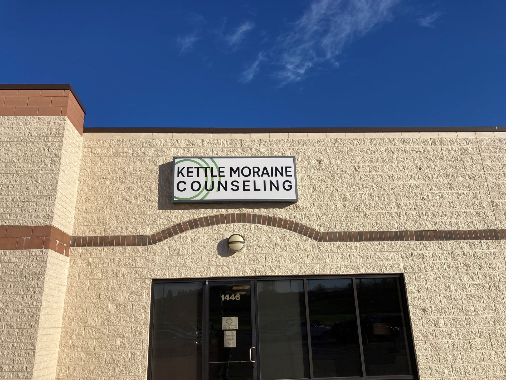 Sign for Kettle Moraine Counseling above a storefront with windows and a blue sky.
