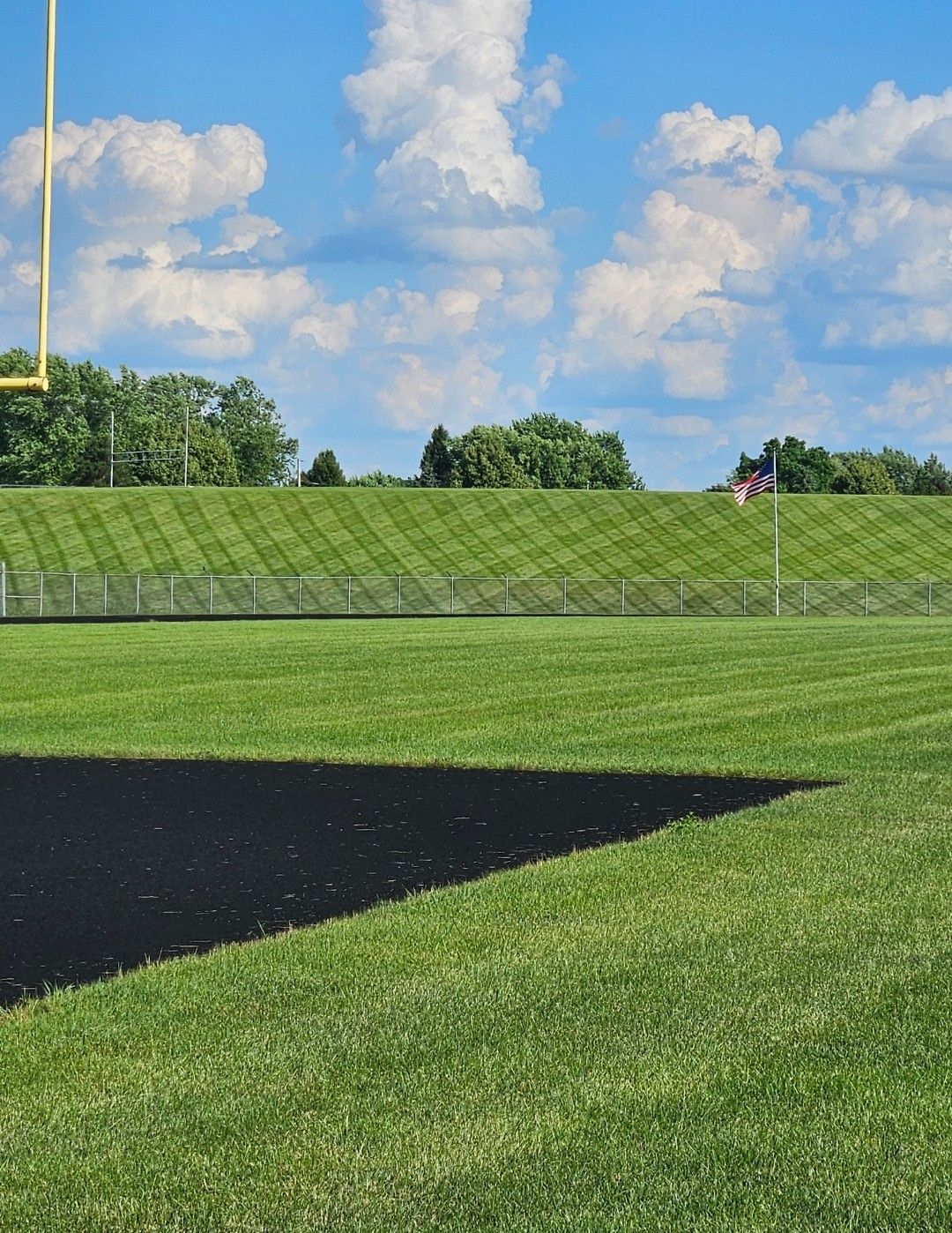Football field with black track, green grass, gold goalpost, and blue sky.