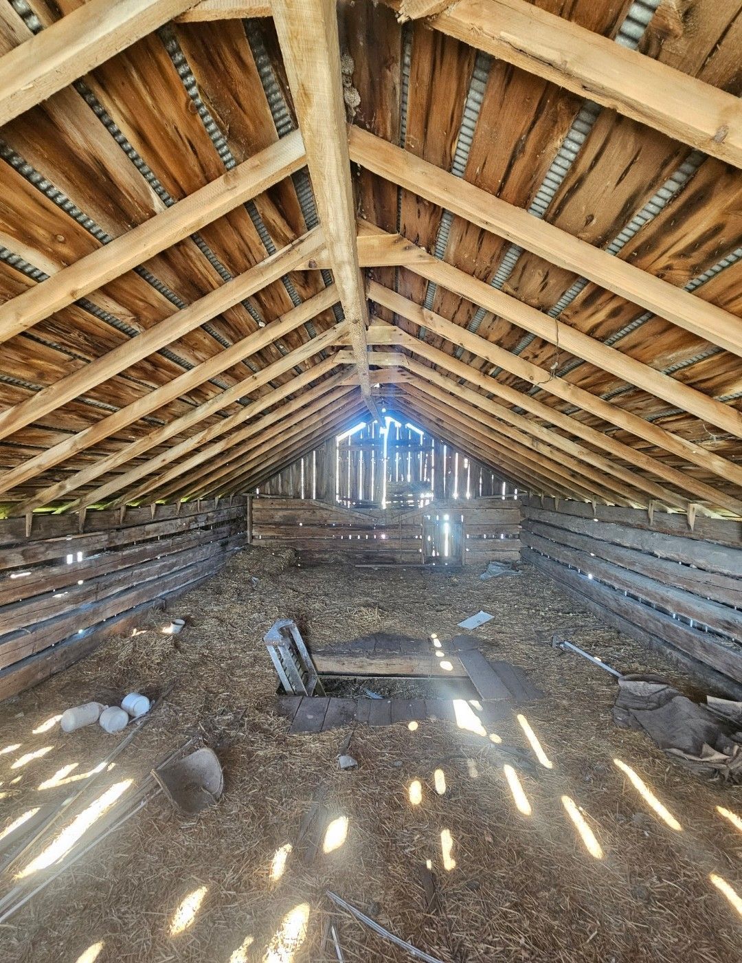 Interior of a dilapidated wooden barn with sunlight streaming through the structure.