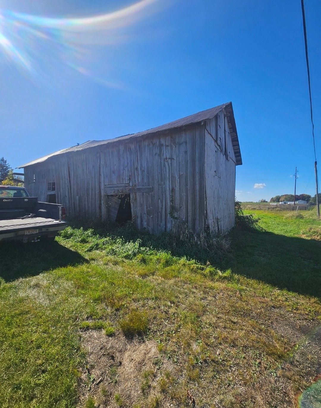 Weathered wooden barn on a grassy field under a bright blue sky.