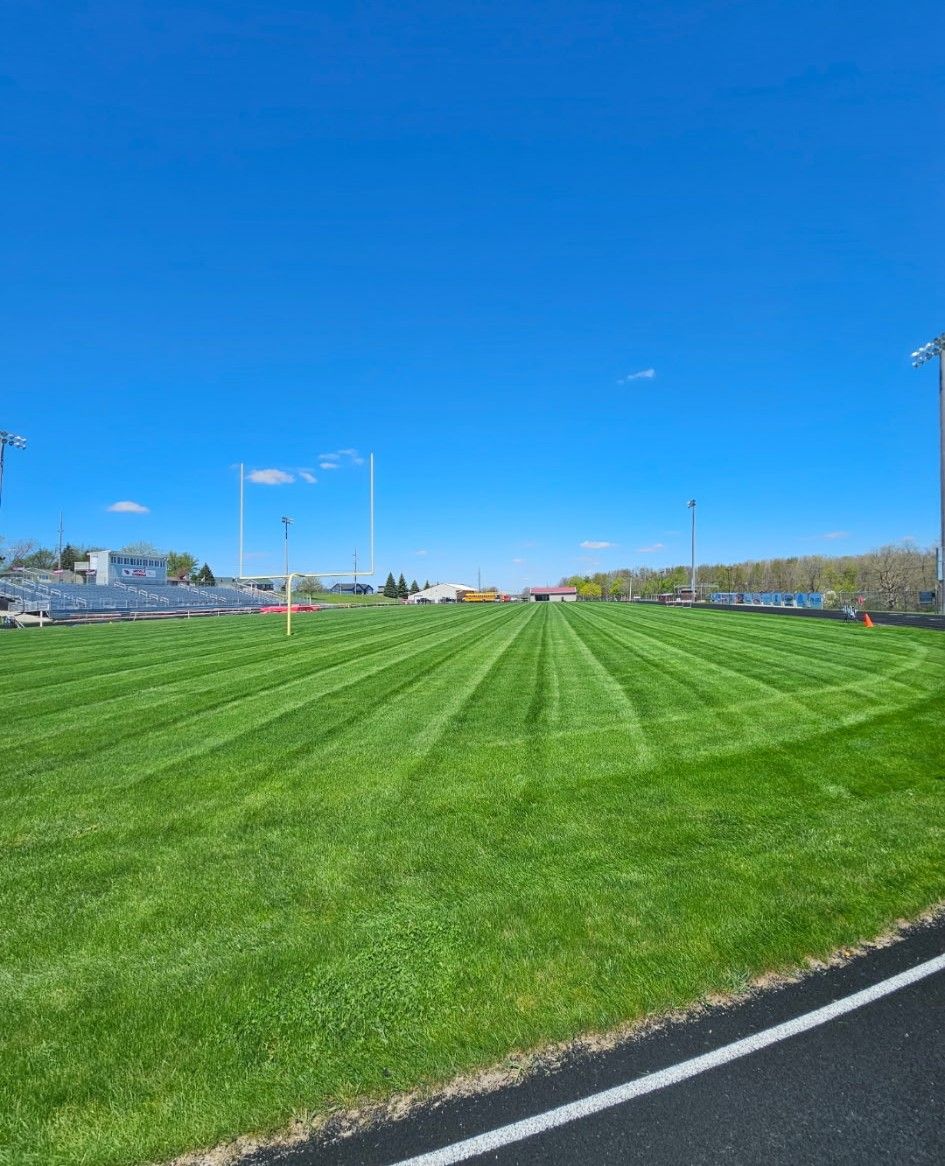 A freshly mowed, striped football field viewed from the track under a clear blue sky.
