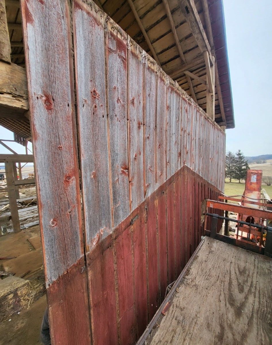 A side view of a weathered barn wall with peeling red paint, showing wood grain on the exposed upper sections.