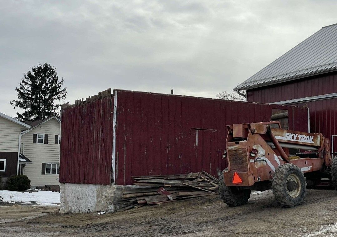 Red barn with weathered wood, concrete base. A lift truck sits nearby. Cloudy sky.