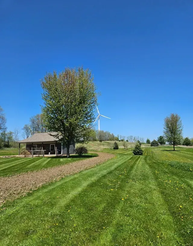 Lawn with a small house, a tree, and a wind turbine under a bright blue sky.