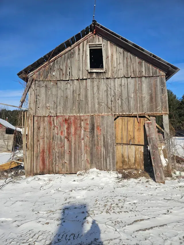 Weathered wooden barn with snow-covered ground and blue sky in the background.