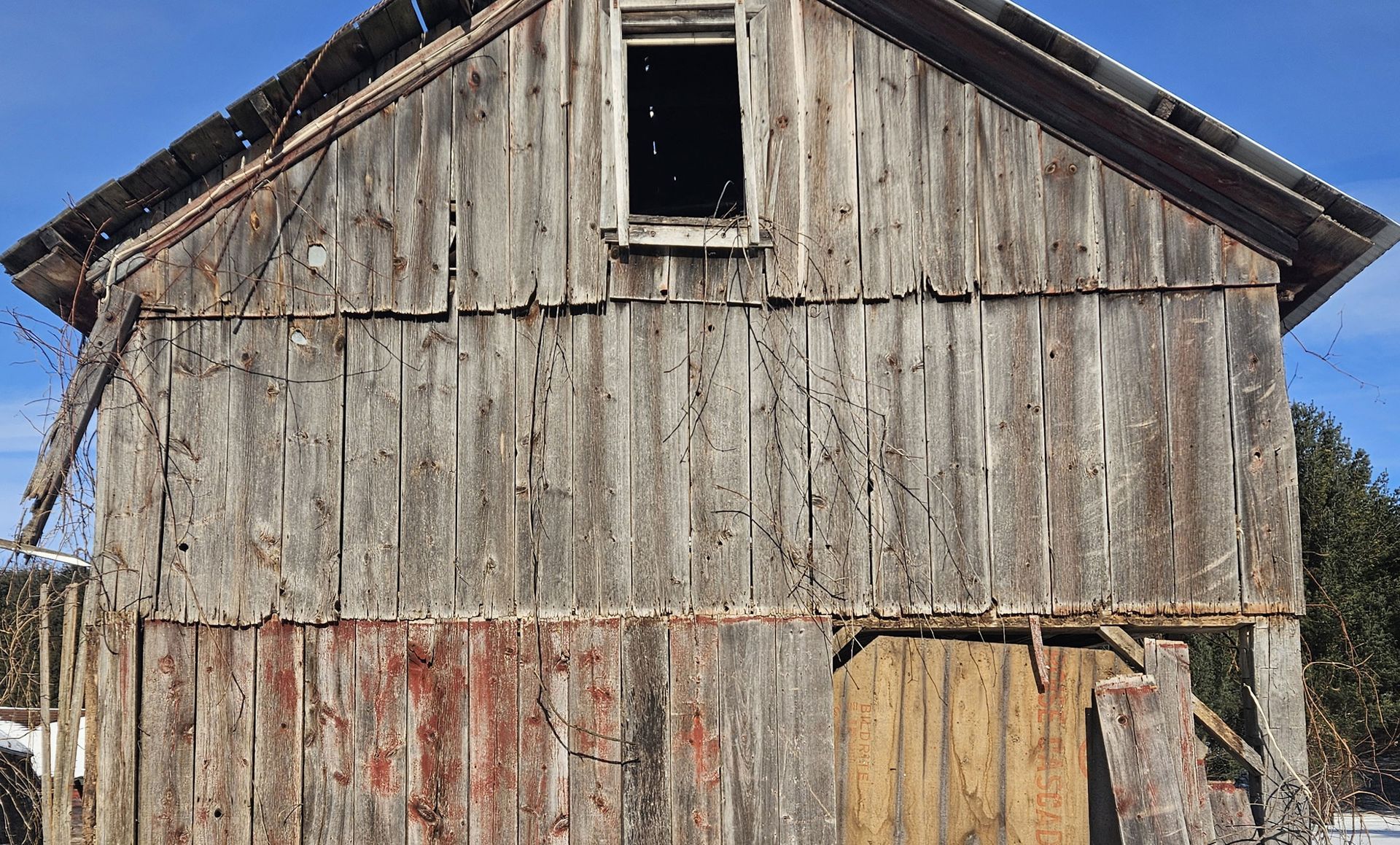 Weathered wooden barn with missing window, exposed roof, and deteriorating boards.