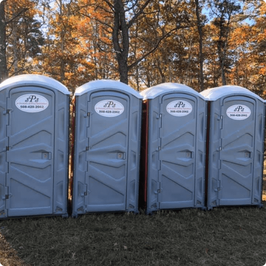 A row of portable toilets in red and gray colors sits on a gravel surface outdoors.