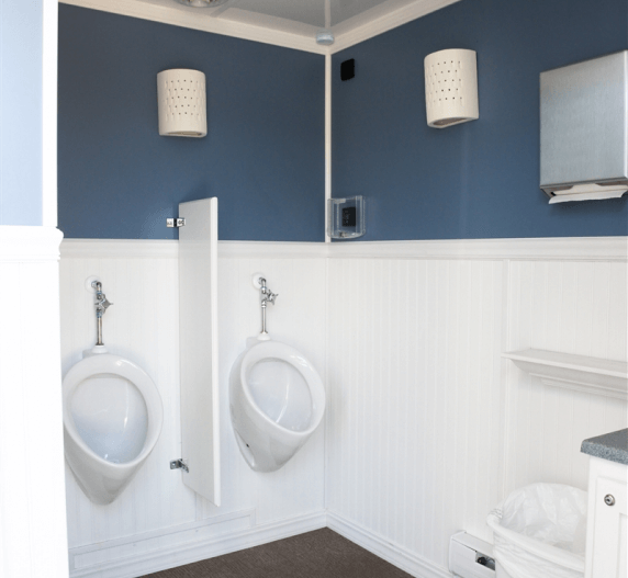 Two urinals in a public restroom with blue and white walls, paper towel dispenser, and wall sconces.