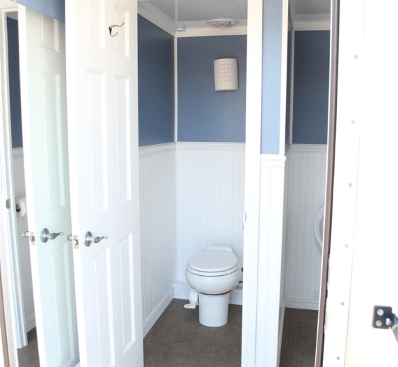 Interior view of a restroom trailer with three private stalls, white and blue walls, and a toilet.