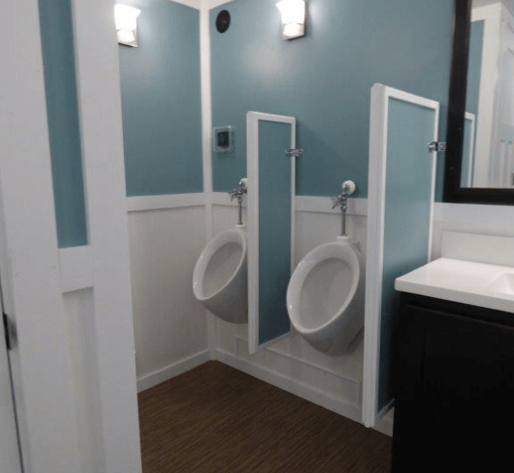 Two urinals in a public restroom with teal walls, white trim, and a black vanity.