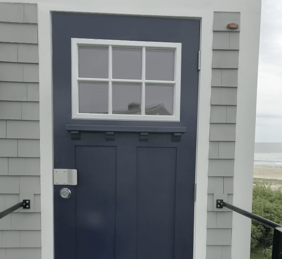 Blue door with six-pane window, white trim, on gray shingle building.