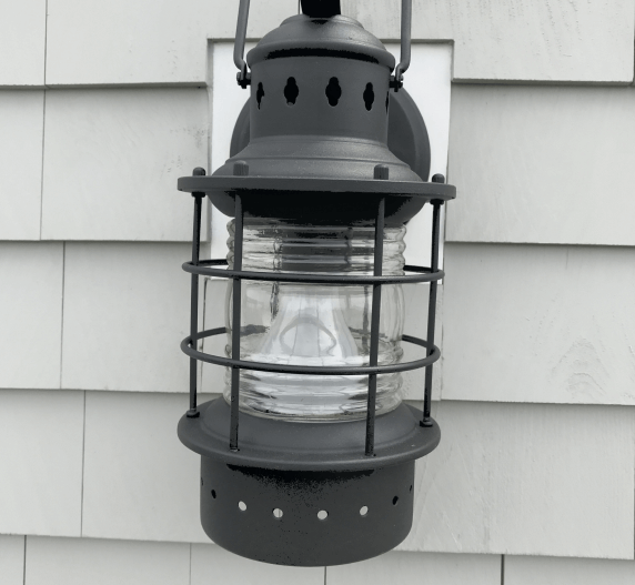 Black nautical-style outdoor wall lantern with glass panels, mounted on gray shingle siding.