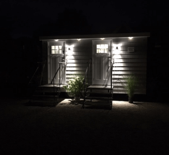Two lit doors on a building at night; each has steps, a light, and a white door with a small window.