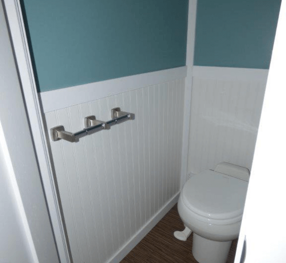 Small bathroom with a white toilet, wainscoting, and teal upper wall; a chrome towel rack is mounted.